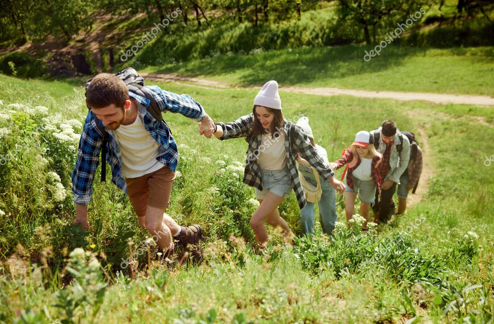 group of young people, friends walking in forest, going hiking on warm sunny day, climbing up the hill, holding hands. support and help